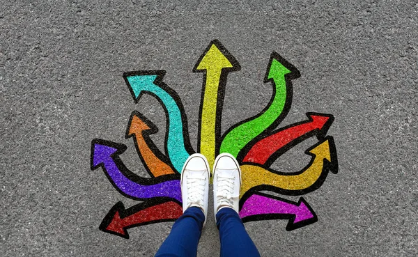 Ayaklar ve oklar yol arka plan üzerinde. Renkli grafiti ok işareti seçenekleri, yaratıcı ve fikir kavramı ile asfalt yolda duran ayak çifti. Selfie kadın beyaz ayakkabı veya spor ayakkabı giyiyor. Üstte görüntü.