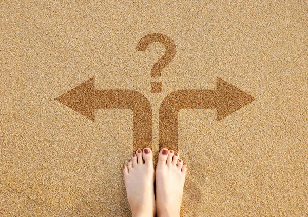 Feet and arrows on sand nature background. Move forward. Woman foot with brown pedicure in beach sand, top view. Barefoot with question mark and two arrows sign, choice concept of making decision.