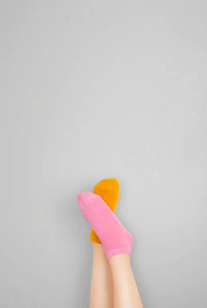 Legs and feet with cute sock. Woman wearing pastel pink and yellow socks raised crossed leg isolated on gray background. Top view. Beauty and fashion concept. Minimalism fashionable winter set.