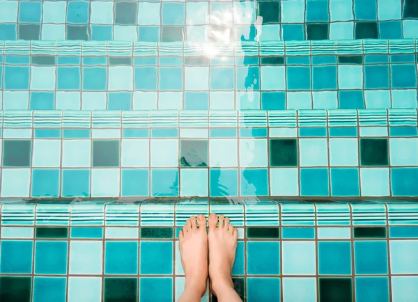 Selfie of feet and legs in green swimming pool and waves background or texture. Top view. Beautiful young female barefoot under aqua water on summer holiday. Woman is wetting toes for relaxing concept.