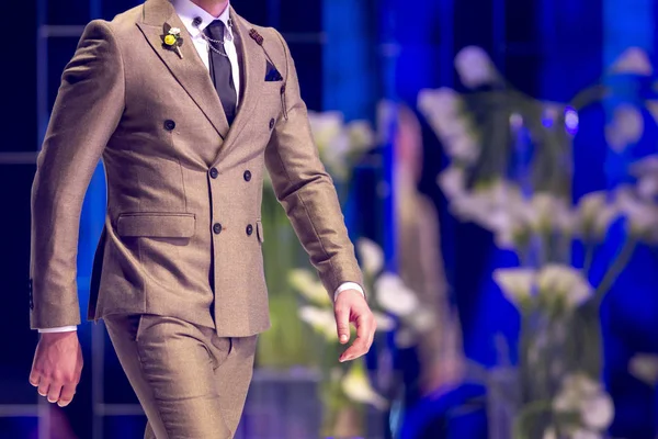 Male model walks the runway in beige suit during a Fashion Show. Fashion catwalk event showing new collection of clothes. Single model.