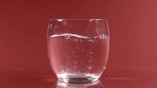 つの赤い反射背景の水のガラスで発泡性の白い錠剤を溶解します スローモーション — ストック動画