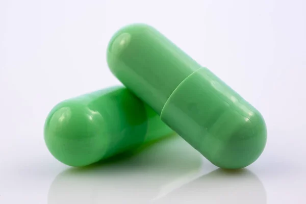 Две Зеленые Капсулы Выделены Белом Отражающем Фоне Мировая Фармацевтическая Промышленность — стоковое фото