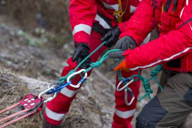 Paramedics from mountain rescue service provide first aid during a training for saving a person in accident in the forest. Unrecognizable people witj ropes and carabiners. clipart