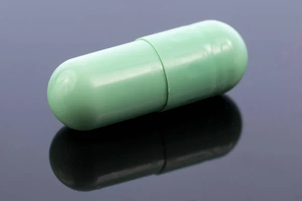 Enkele Groene Capsule Geïsoleerd Zwart Reflecterend Oppervlak Wereldwijde Farmaceutische Industrie — Stockfoto