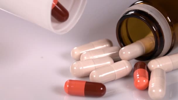 红色和米色胶囊 棕色和白色瓶落在白色反光表面 全球制药业每年花费数十亿美元 慢动作 — 图库视频影像