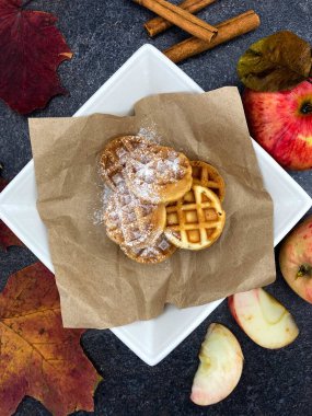 Taze pişmiş Viyana waffleları üzerine toz şeker serpiştirilmiş taze kırmızı elmalar ve koyu taştan bir yüzeye aromatik tarçın serpiştirilmiş..
