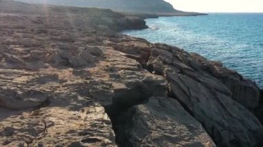 Akdeniz adasının taşlı sahillerindeki deniz mağaraları, ağır çekim, insansız hava aracının görüntüsü