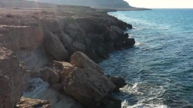 Akdeniz adasının taşlı sahillerindeki deniz mağaraları, ağır çekim, insansız hava aracının görüntüsü