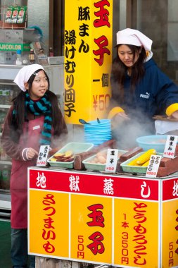 Beppu, Japonya - 29 Aralık 2009: İki genç kız açık hava pazarında yemek pişiriyor. Haşlanmış yumurta, mısır ve patates popüler bir fast food..