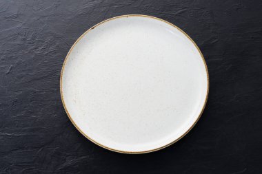 Boş beyaz seramik tabaklar, kaşıklar ve çatallar eski siyah tahta bir masaya dizilmiş..