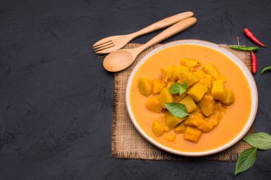 Siyah arkaplana yerleştirilmiş kaşık ve çatalla seramik bir tabakta servis edilen köri ya da balkabağı çorbası - mesaj yazmak için alan ile üst görünüm.