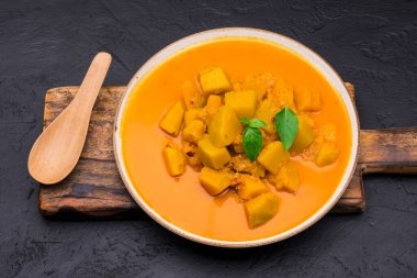 Siyah arkaplana yerleştirilmiş kaşık ile seramik tabakta servis edilen köri ya da balkabağı çorbası - mesaj yazmak için alan ile üst görünüm.