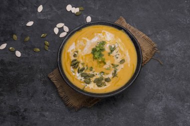 Siyah zemin üzerinde seramik tabakta servis edilen pirinçli köri ya da balkabağı çorbası..