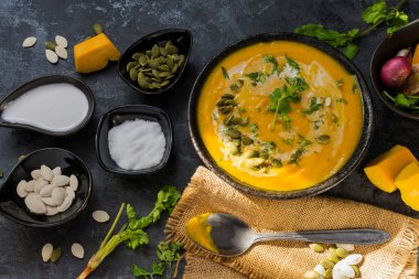 Siyah zemin üzerinde seramik tabakta servis edilen pirinçli köri ya da balkabağı çorbası..