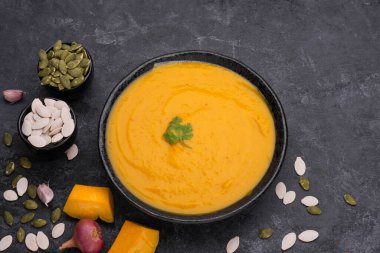 Siyah zemin üzerinde seramik tabakta servis edilen pirinçli köri ya da balkabağı çorbası..