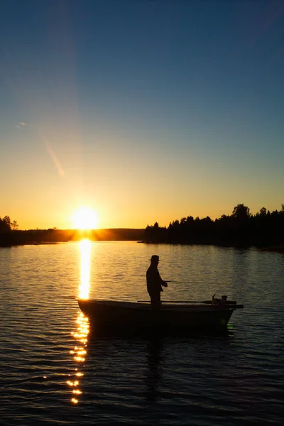 立っていると日没で小さな湖で手漕ぎボートでの釣り人のシルエット画像 — ストック写真
