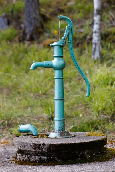Vintage green hand operated water pump above its well.