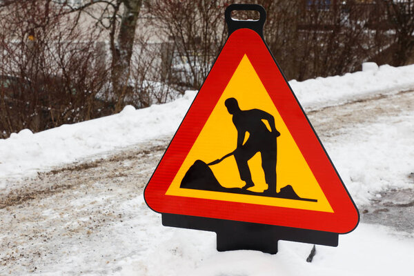 Roadwork warning sign at a snow road during the winter season.