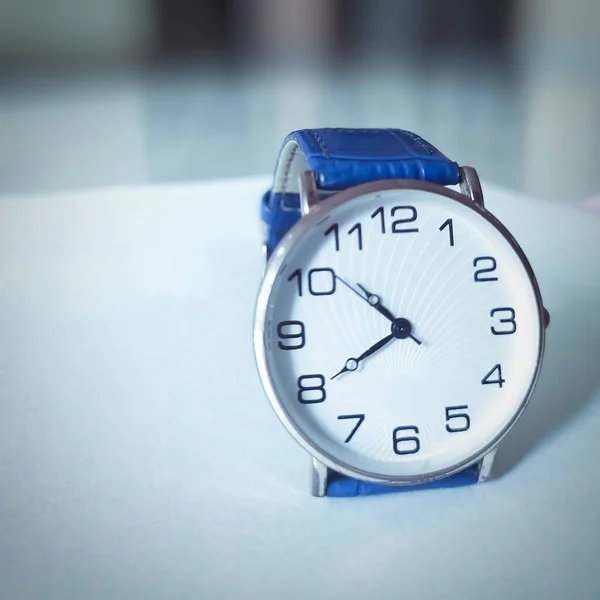 Beyaz zemin üzerinde mavi kuşaklı kol saati..