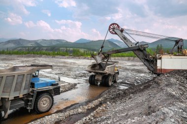 Altın madenciliği endüstrisi. Bu kütlelerden daha fazla doğal altın çıkarmak için çöp kamyonları çıkartarak bir kazı kovası ve altın taşıyan dağ toprağının taşınması. Doğu Sibirya