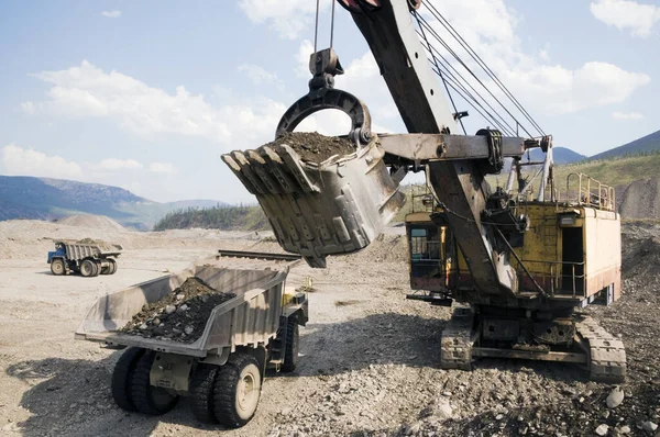 Gold mining industry. Loading with an excavator bucket and transportation of gold-bearing mountain soil by mining dump trucks in order to further extract natural gold from this mass. Eastern Siberia