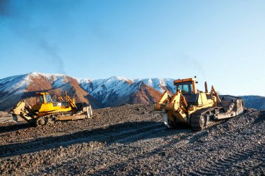  Dağlık bölgelerdeki buldozerler, katman katman, dağ toprağını yüzeyden çıkarıp kenara doğru kürekliyorlar..