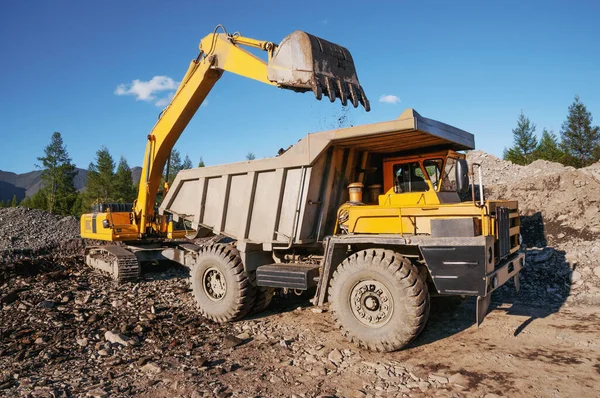 A mining dump truck in the highlands. The excavator loads the mountain soil with a bucket into the body of a dump truck