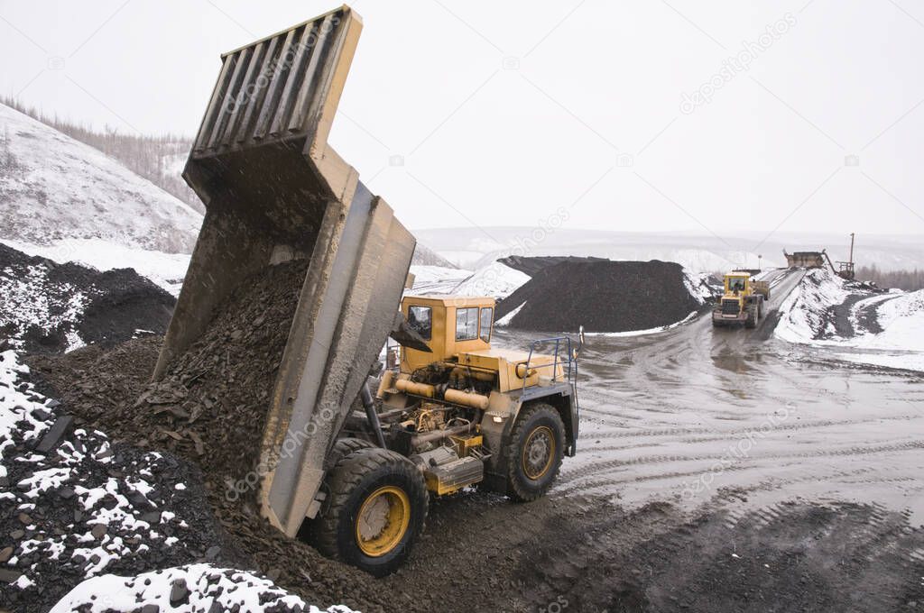  Excavation work in the highlands at the beginning of winter. A mining dump truck unloads mountain soil
