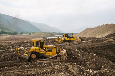 Dağlık bir orman bölgesinde doğal altın madenciliği. Buldozerler, güneşli bir yaz gününde bir dağ ormanında çalışma sürecinde.