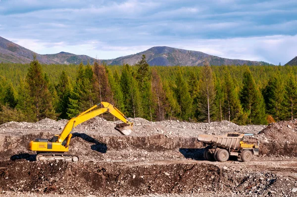 Kazı makinesi kullanarak bir maden kamyonunun cesedine dağ toprağı yüklemek ve kargoyu daha fazla taşımak. Doğu Sibirya 'nın dağlık bölgesinde minerallerin çıkarılması 