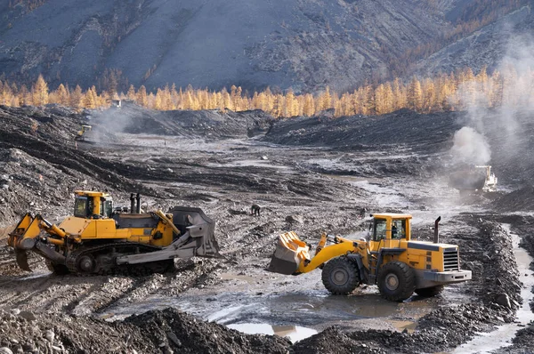 Open pit mining natural gold in mountainous areas Bulldozer collects heap of mountain soil in which there is increased concentration of natural gold (Aurum). Then, wheel loaders transport this mountain soil to special industrial equipment for washing