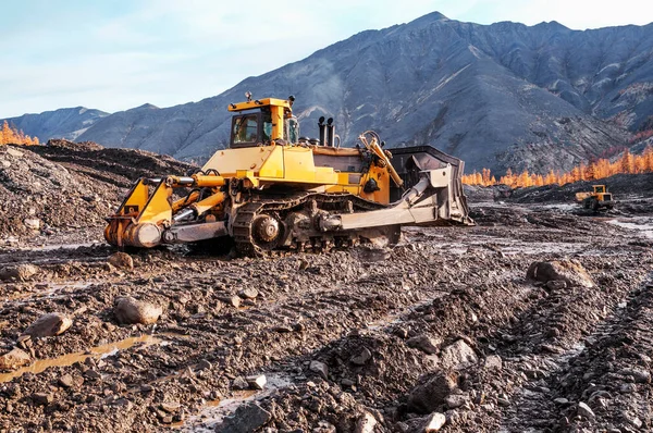 Buldozer dağ toprağını zapt eder ve sonra da sanayi kovası ile üst katmanı kaldırır. Sibirya 'nın dağlık bölgelerinde minerallerin çıkarılması (altın madenciliği) 