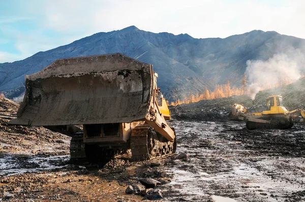 Bulldozer in a mountainous area in an industrial area, with an industrial bucket raised to the top