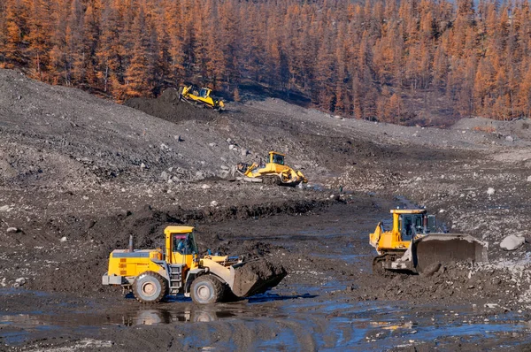 Open pit mining natural gold in mountainous areas Bulldozer collects heap of mountain soil in which there is increased concentration of natural gold (Aurum). Then, wheel loaders transport this mountain soil to special industrial equipment for washing