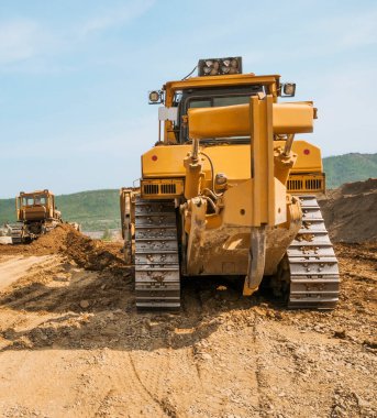 Güneşli bir yaz gününde açık bir alanda toprak işleri. Kargo kamyonları, kazıcılar, tekerlek yükleyiciler ve buldozerler aynı anda çalışır..