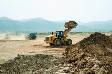 Tekerlek yükleyicisi bir çöp kamyonunun kovasına kil yükler.