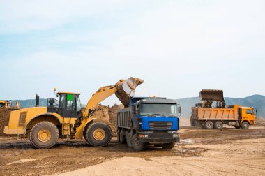 Tekerlek yükleyicisi bir çöp kamyonunun kovasına kil yükler.