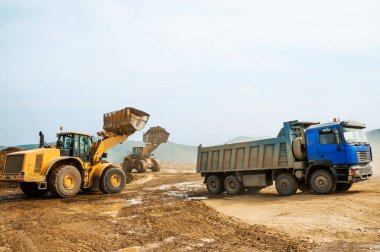 Tekerlek yükleyicisi bir çöp kamyonunun kovasına kil yükler.
