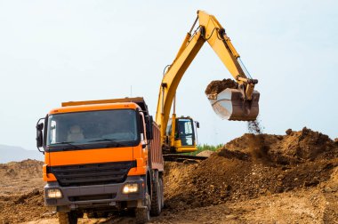 Kazıcı, güneşli bir yaz gününde bir çöp kamyonunun içine kil doldurur.