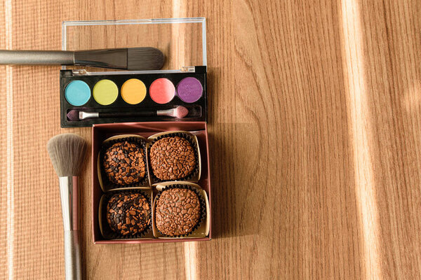 Коробка с четырьмя бригальтерами, кисточками и макияжем, освещаемыми лучом солнца.