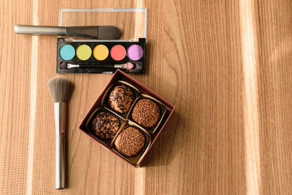 Коробка с четырьмя бригальтерами, кисточками и макияжем, освещаемыми лучом солнца (вид сверху)).