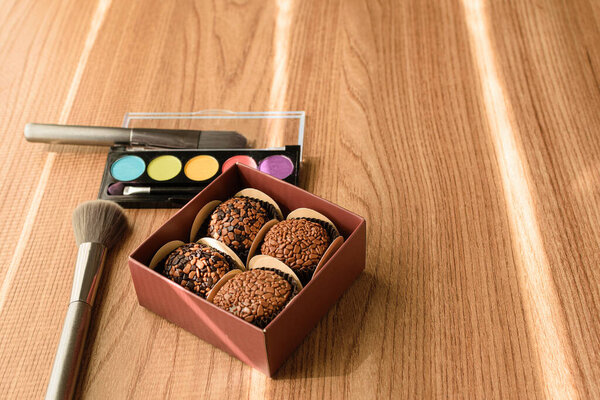 На переднем плане коробка с бригадирами. Фоновый макияж и кисти (вид сбоку).