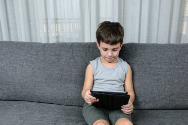 7 yaşında, masum yüzlü, tableti izleyen bir çocuk..