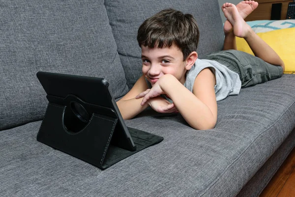 7 yaşında bir çocuk, kanepede uzanmış, elinde tekneyle ve yaramaz bir suratla..