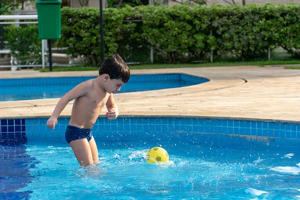 Havuzdaki çocuk topa vurmaya hazırlanıyor.