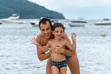 Baba ve oğul sahilde fotoğraf için poz veriyorlar.