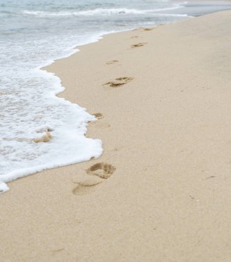 Sahildeki kumların üzerindeki insan ayak izleri deniz dalgası tarafından siliniyor..