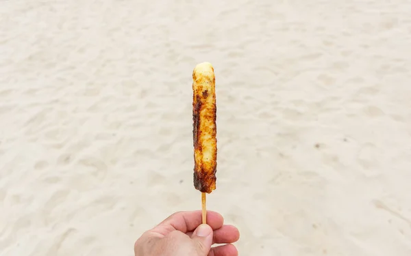 Bir kürdana eklenmiş peynir kavurması (arka planda kumsal kumu)).