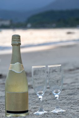 Bir şişe şampanya ve kumsalın kumlarında iki bardak yakın plan (dikey fotoğraf)).
